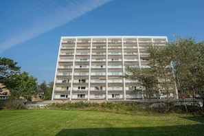 Ein mehrstöckiges Wohngebäude mit Balkonen, einer flachen Dachterrasse und blauem Himmel.