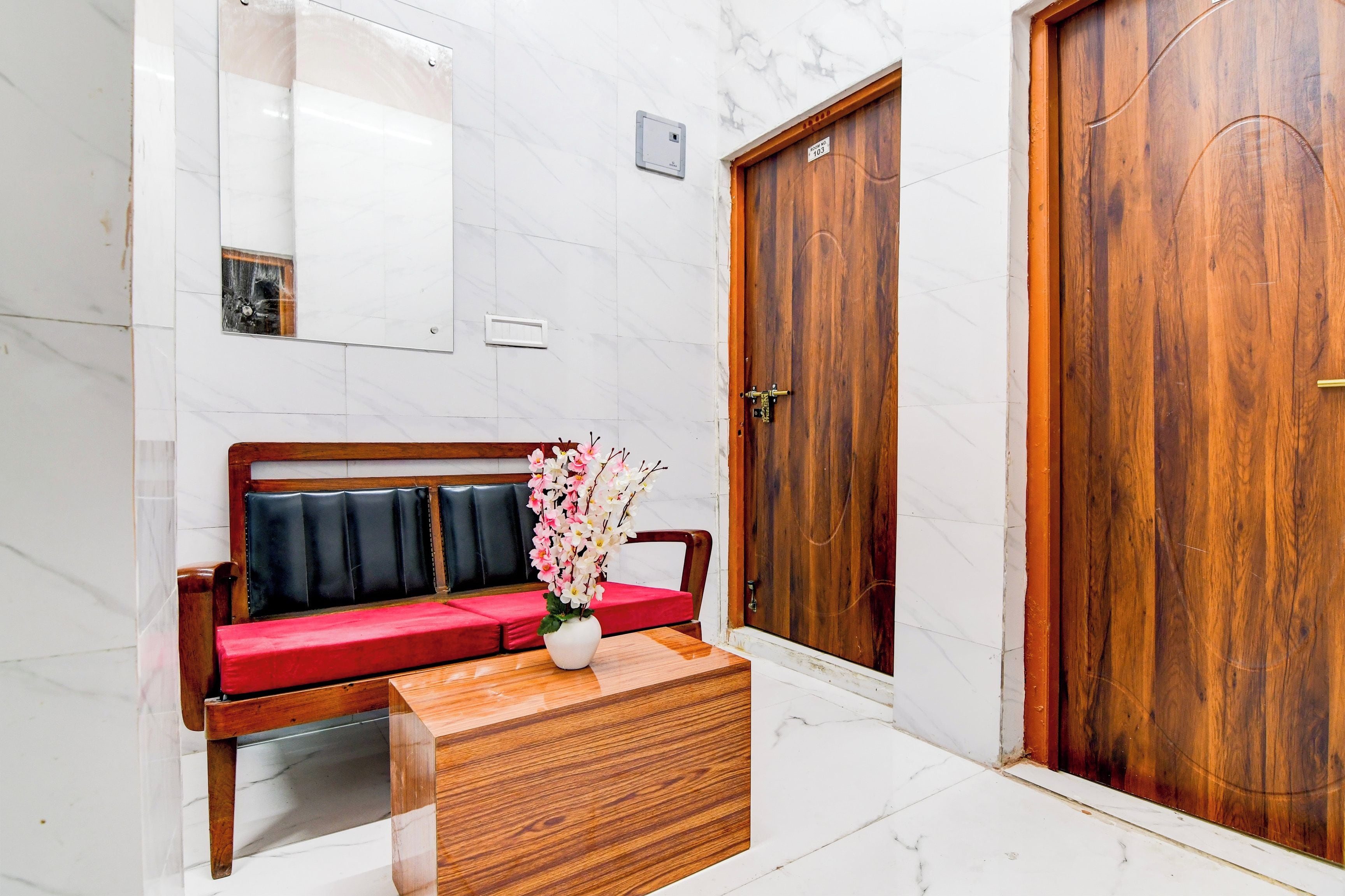 A hotel lobby with a wooden bench, a vase with flowers, and two wooden doors.