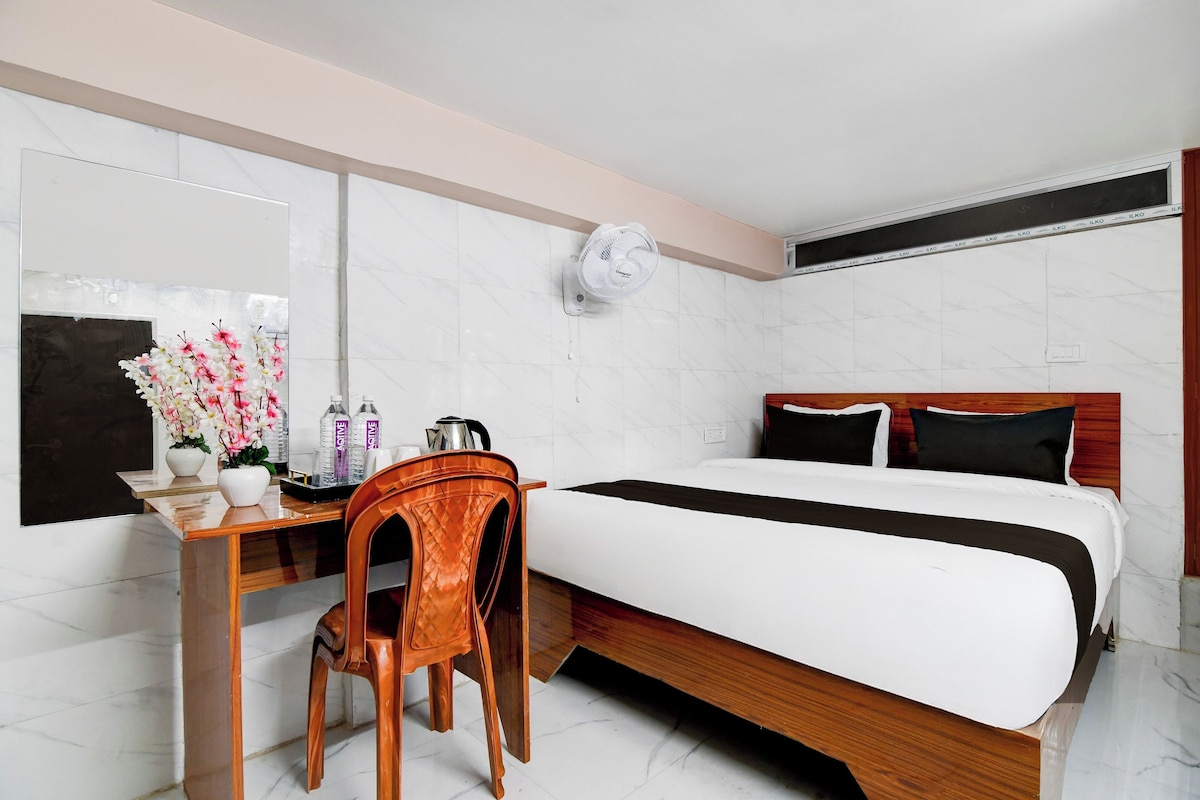 Habitación de hotel con cama, escritorio, silla, espejo y ventilador de pared.