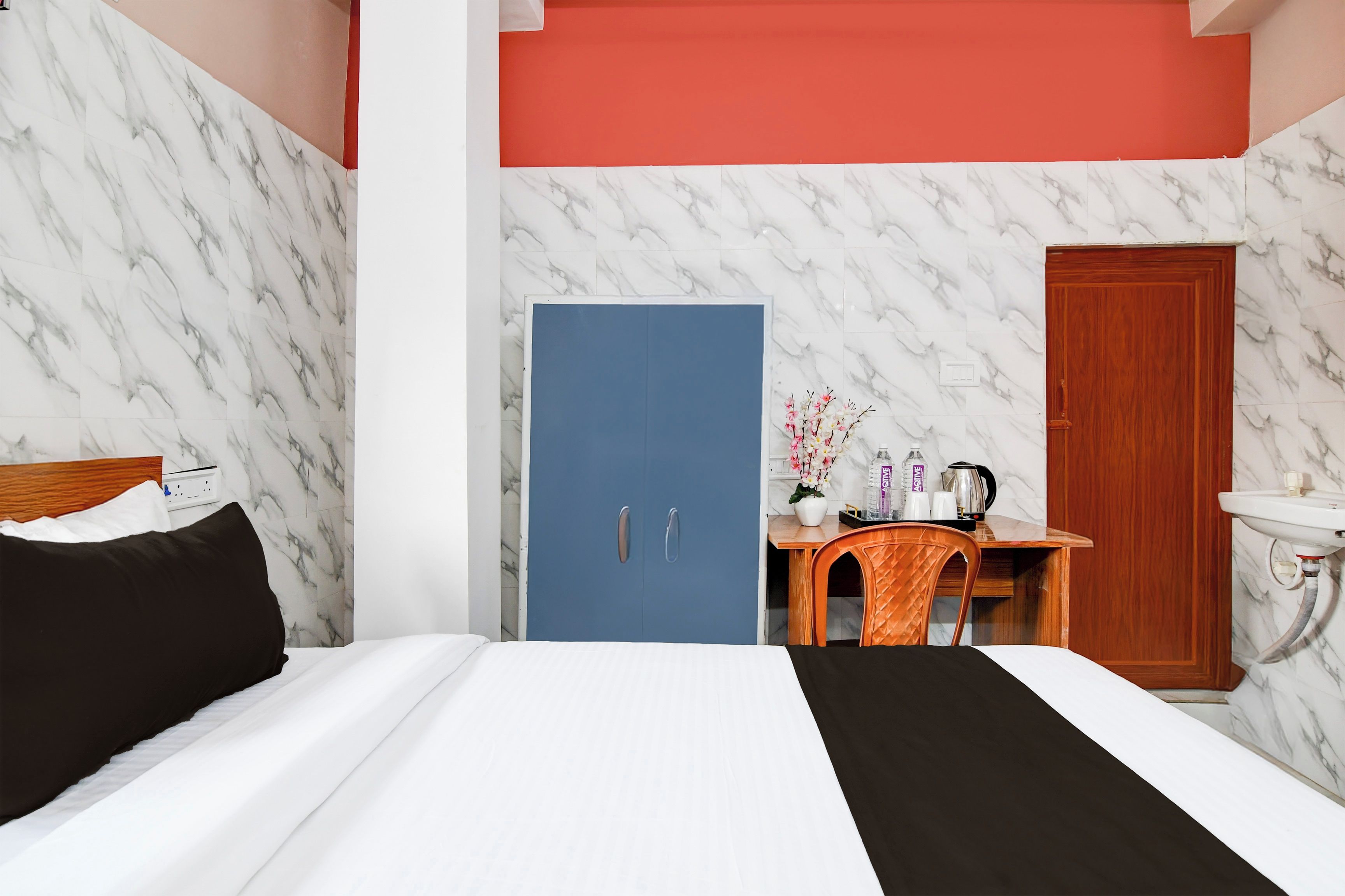 A hotel room with a bed, a desk with a chair, a wooden wardrobe, and a bathroom with a sink.
