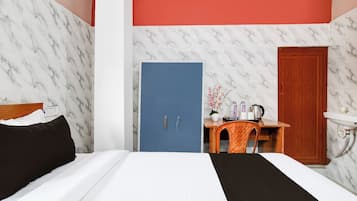 A hotel room with a bed, a desk with a chair, a wooden wardrobe, and a bathroom with a sink.