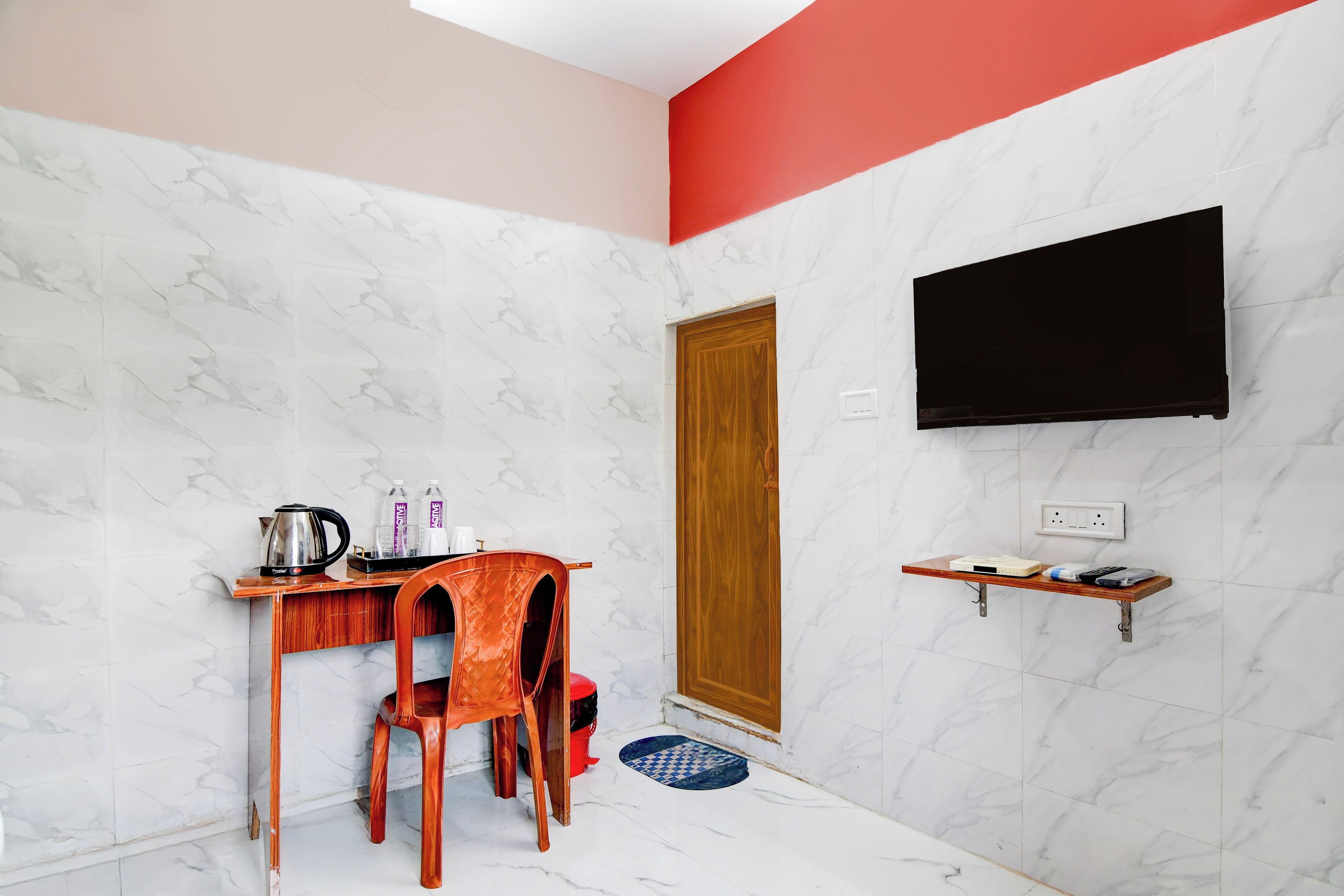Una habitación pequeña con un escritorio de madera, una silla, un televisor montado en la pared y una pequeña estantería.