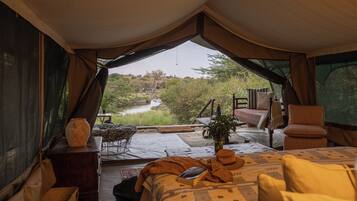 Alojamento em tenda com cama, mesa e vista para um rio.