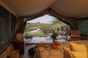 A tented accommodation with a bed, a table, and a view of a river.