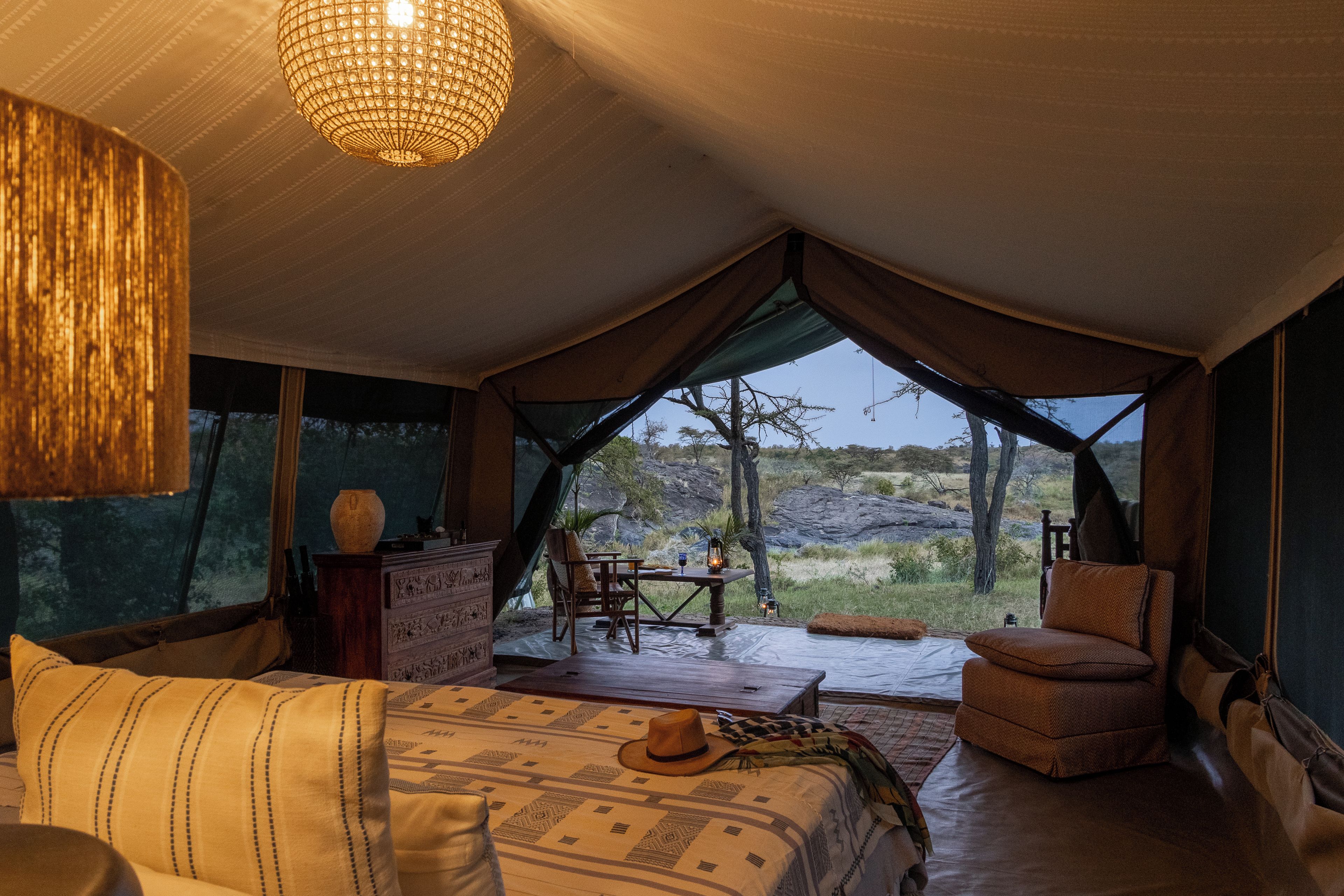 A tented accommodation with a bed, seating area, and a view of the outdoors.