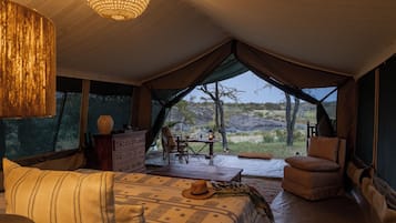 A tented accommodation with a bed, seating area, and a view of the outdoors.
