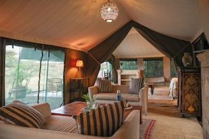 A tented accommodation with a lounge area, a table with a vase, and a view of the outdoors.