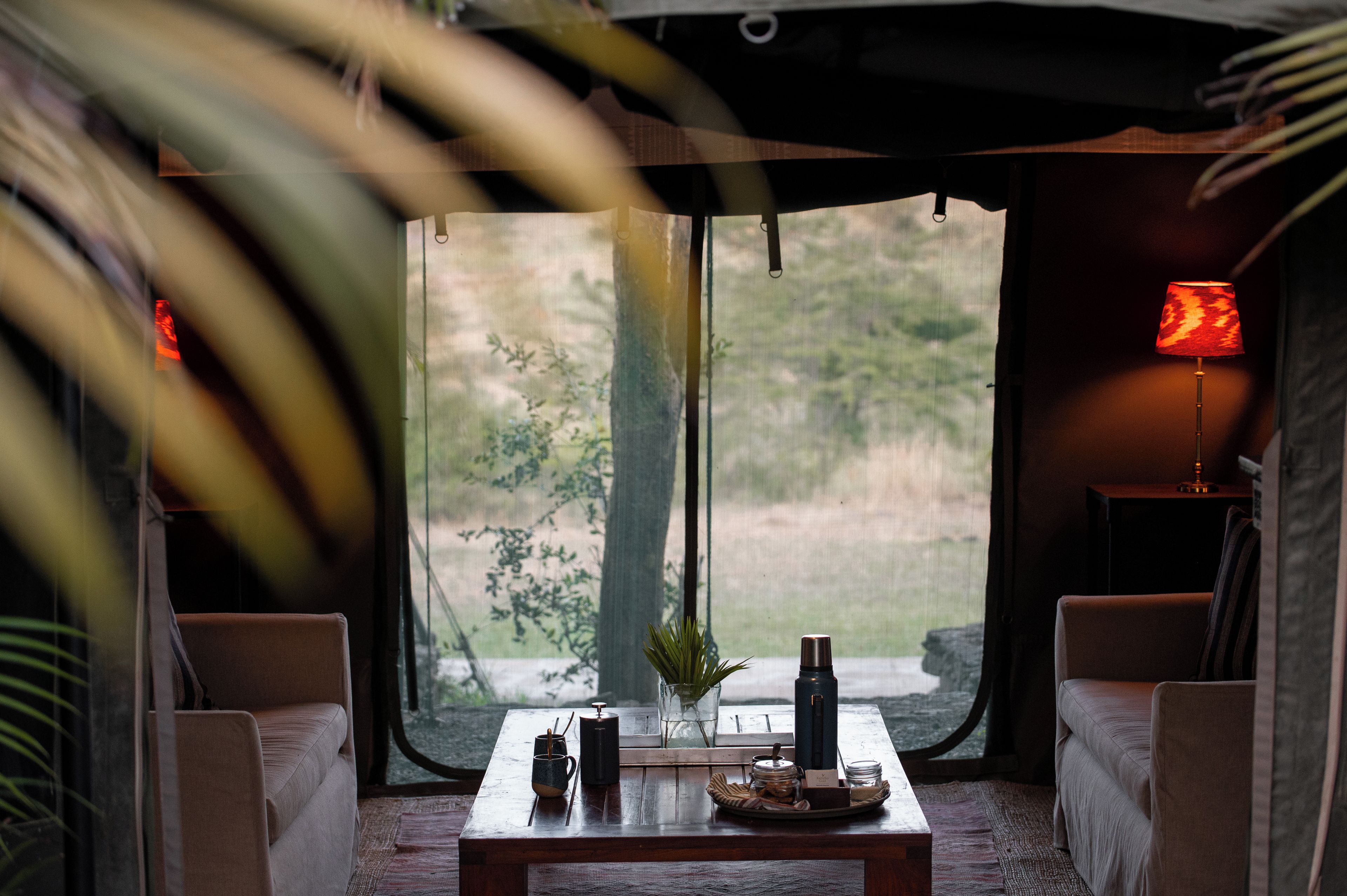 Um quarto aconchegante com uma mesa posta para o chá, uma luminária e vista para o verde lá fora.