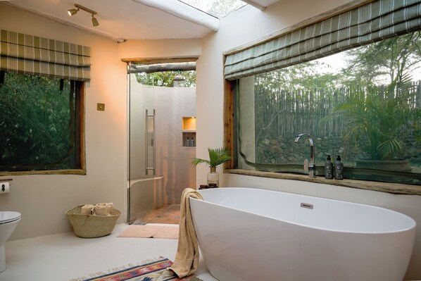 A bathroom with a freestanding bathtub, a toilet, a shower area, and a window with a view of greenery.
