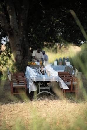 An outdoor dining area with a table set for a meal, surrounded by chairs and a bench.