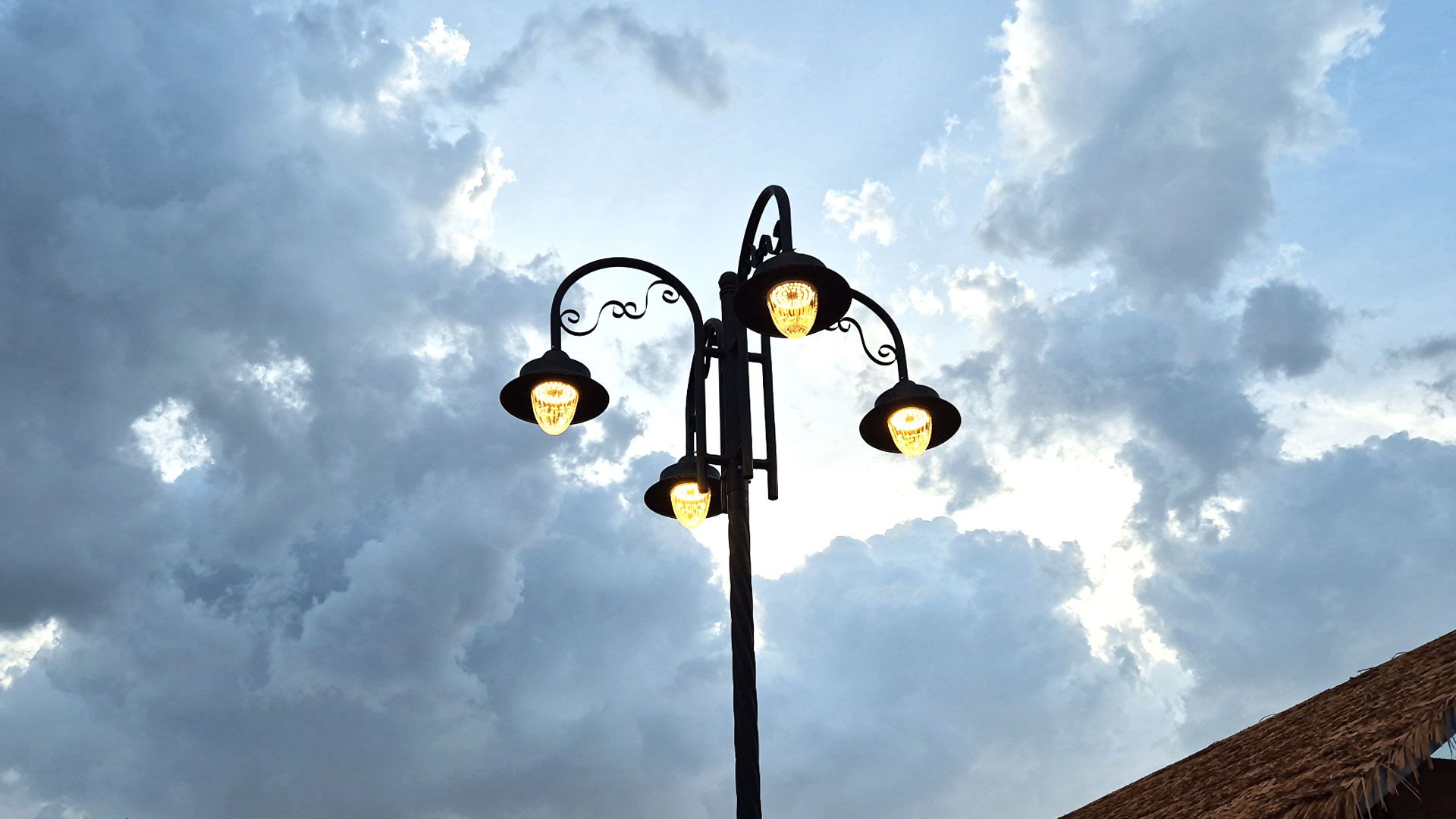 Un farol con tres luces al fondo de un cielo nublado.
