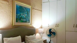 A hotel room with a bed, pillows, a nightstand, a lamp, a fan, and a wardrobe. - Adam's central stay in Saltriver Cape Town (Cape Town)