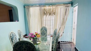 A dining area with a glass table and patterned chairs, a vase of flowers, and a view through a curtained window. - Adam's central stay in Saltriver Cape Town (Cape Town)