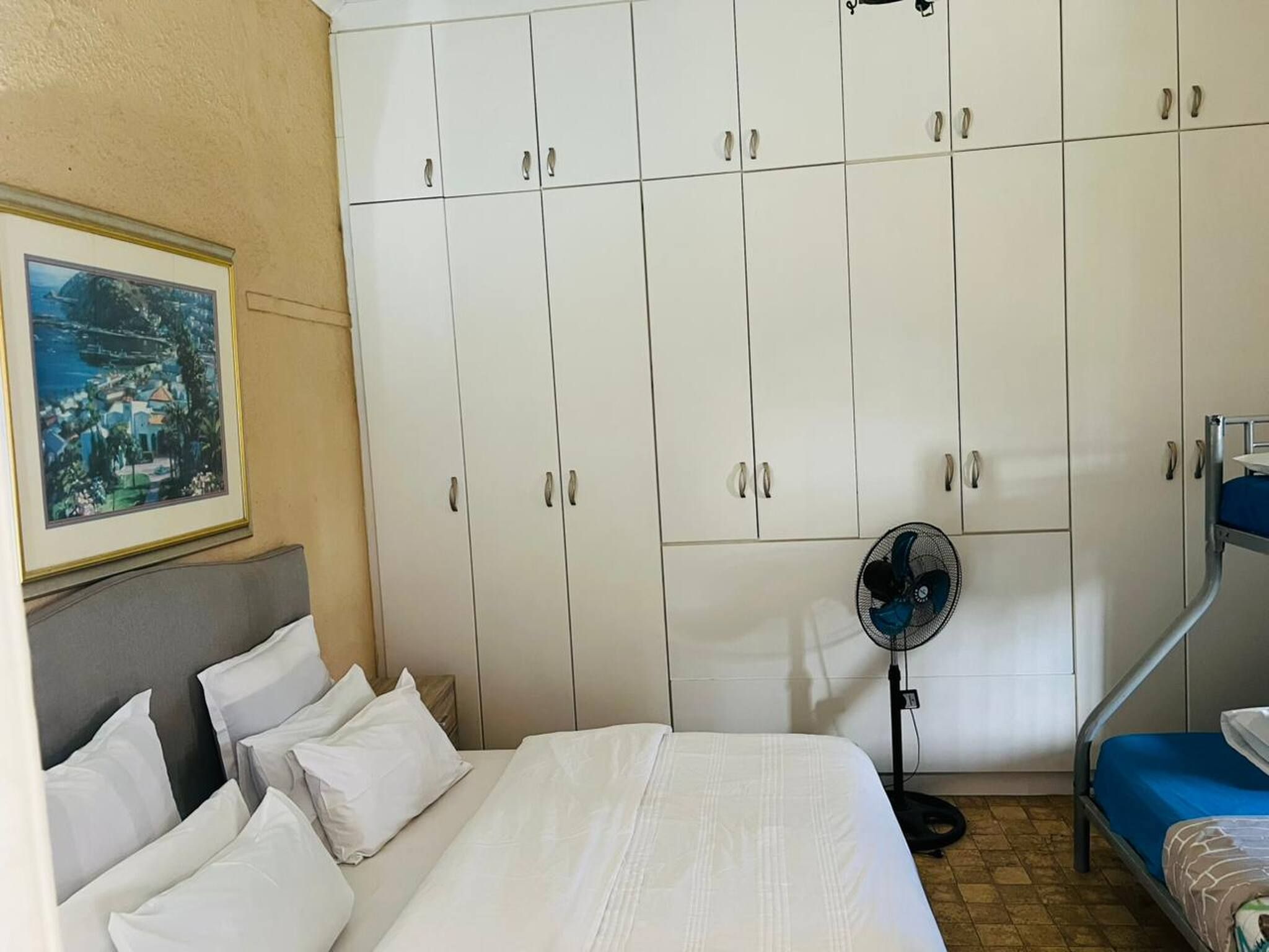A hotel room with a bed, a fan, and a wardrobe.