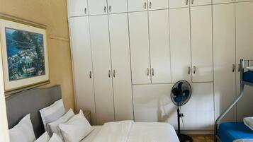 A hotel room with a bed, a fan, and a wardrobe.