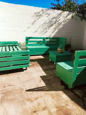 A patio area with green furniture, including a bench and a table, against a white wall.