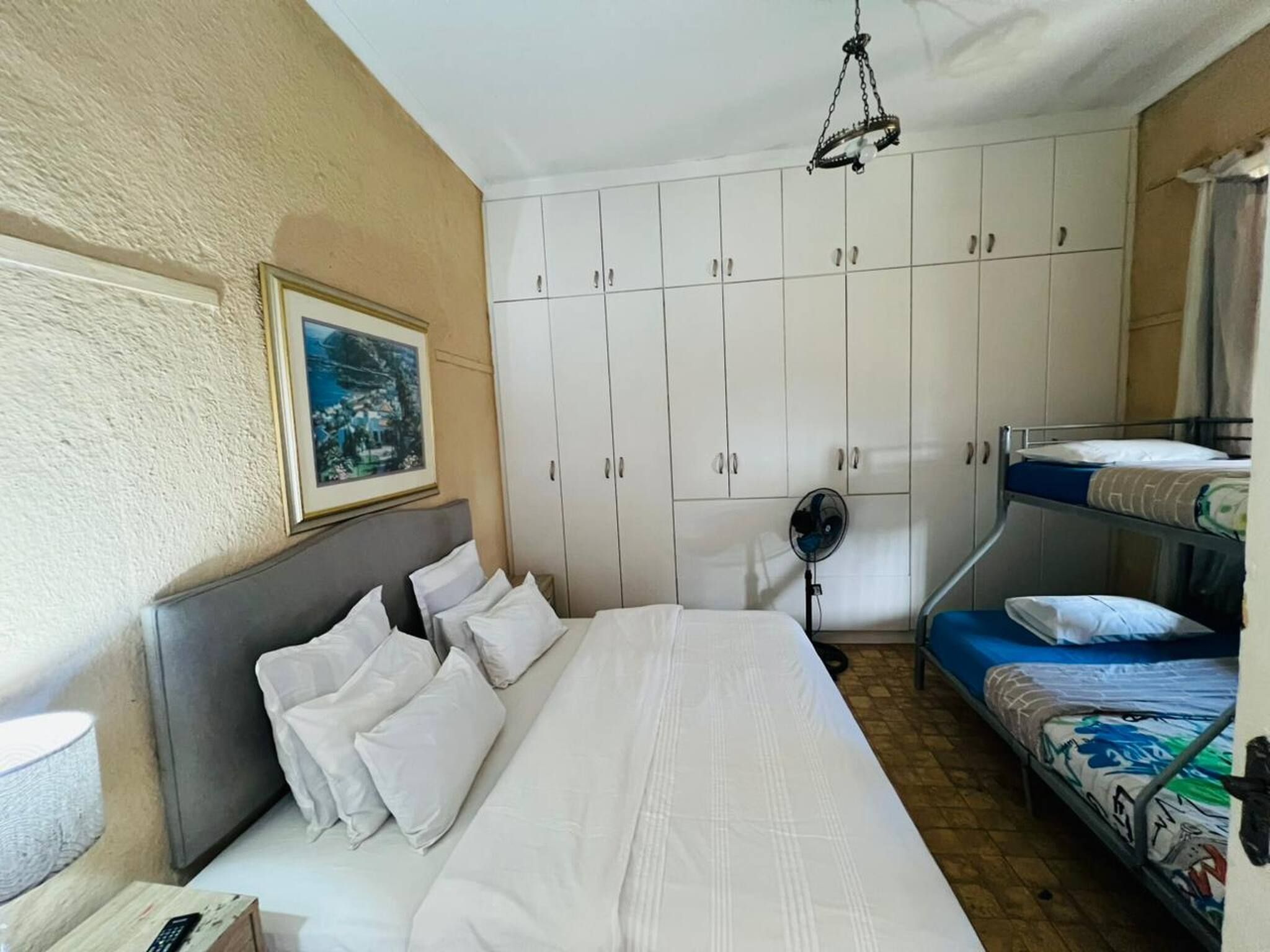 Een slaapkamer met een enkel bed, een stapelbed, een plafondventilator en een ingelijst schilderij aan de muur.