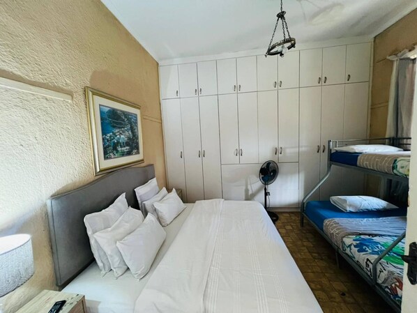 A bedroom with a single bed, a bunk bed, a ceiling fan, and a framed picture on the wall.