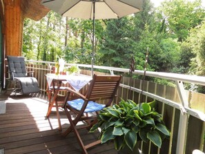 A wooden deck with a table and chairs, a hanging umbrella, and a railing overlooking a forested area. - Holiday Apartment With 1 Bedroom (Born auf dem Darss)