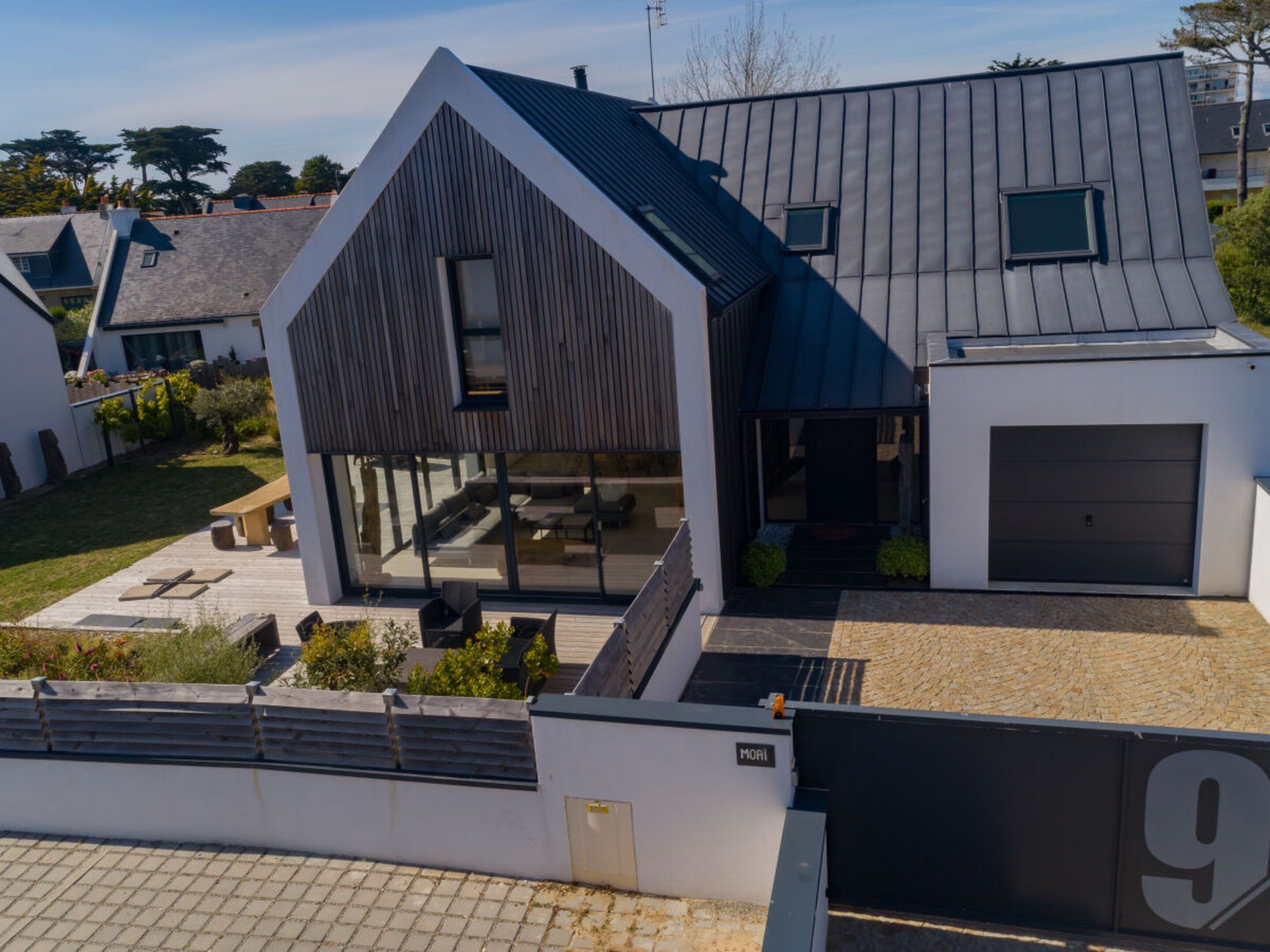 A modern house with a large garage, a covered outdoor seating area, and a well-maintained garden.