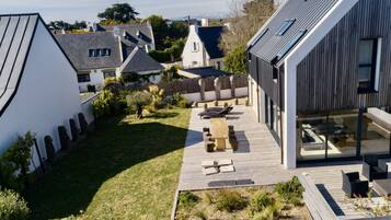 A modern house with a wooden deck, a swimming pool, and a garden.