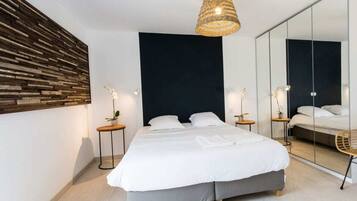 A modern bedroom with a large bed, a dark accent wall, a woven light fixture, and a full-length mirror.