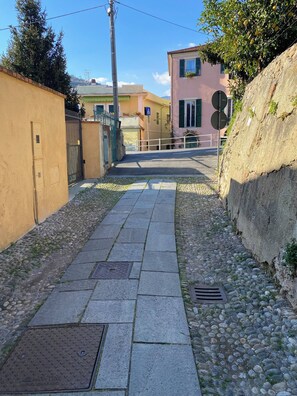 Ein schmaler Steinweg führt zu einem Gebäude mit einer rosafarbenen Fassade und einem Metallgitter.