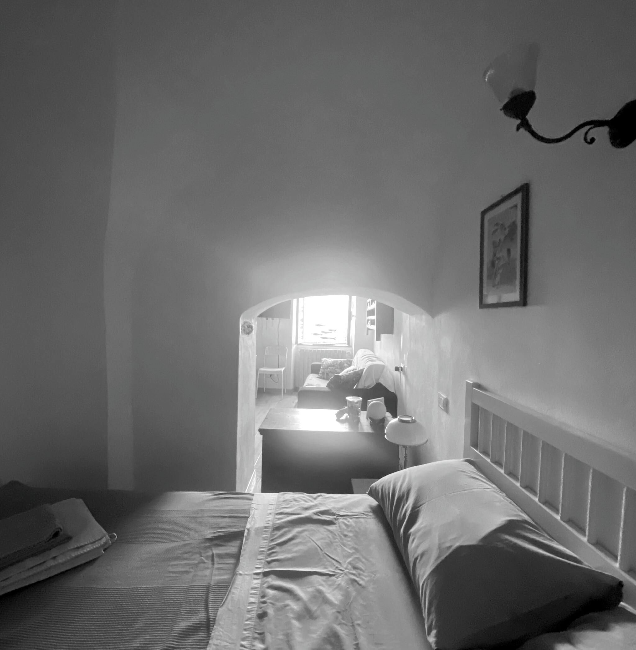 A monochrome room with a bed, a chair, a table, and a lamp.