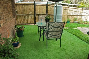 Une terrasse avec du gazon synthétique, une table et deux chaises.