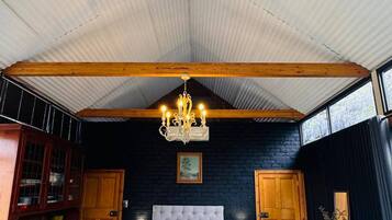 A bedroom with a large bed, a chandelier, wooden beams, a dark brick wall, and a window.