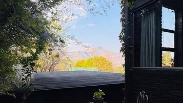 Une terrasse avec une table et des chaises, entourée de verdure et offrant une vue sur des collines lointaines.
