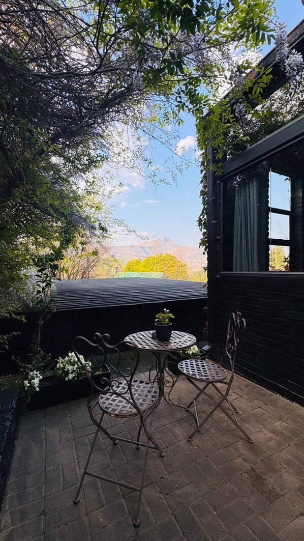 A patio with a table and chairs, surrounded by greenery and a view of distant hills.