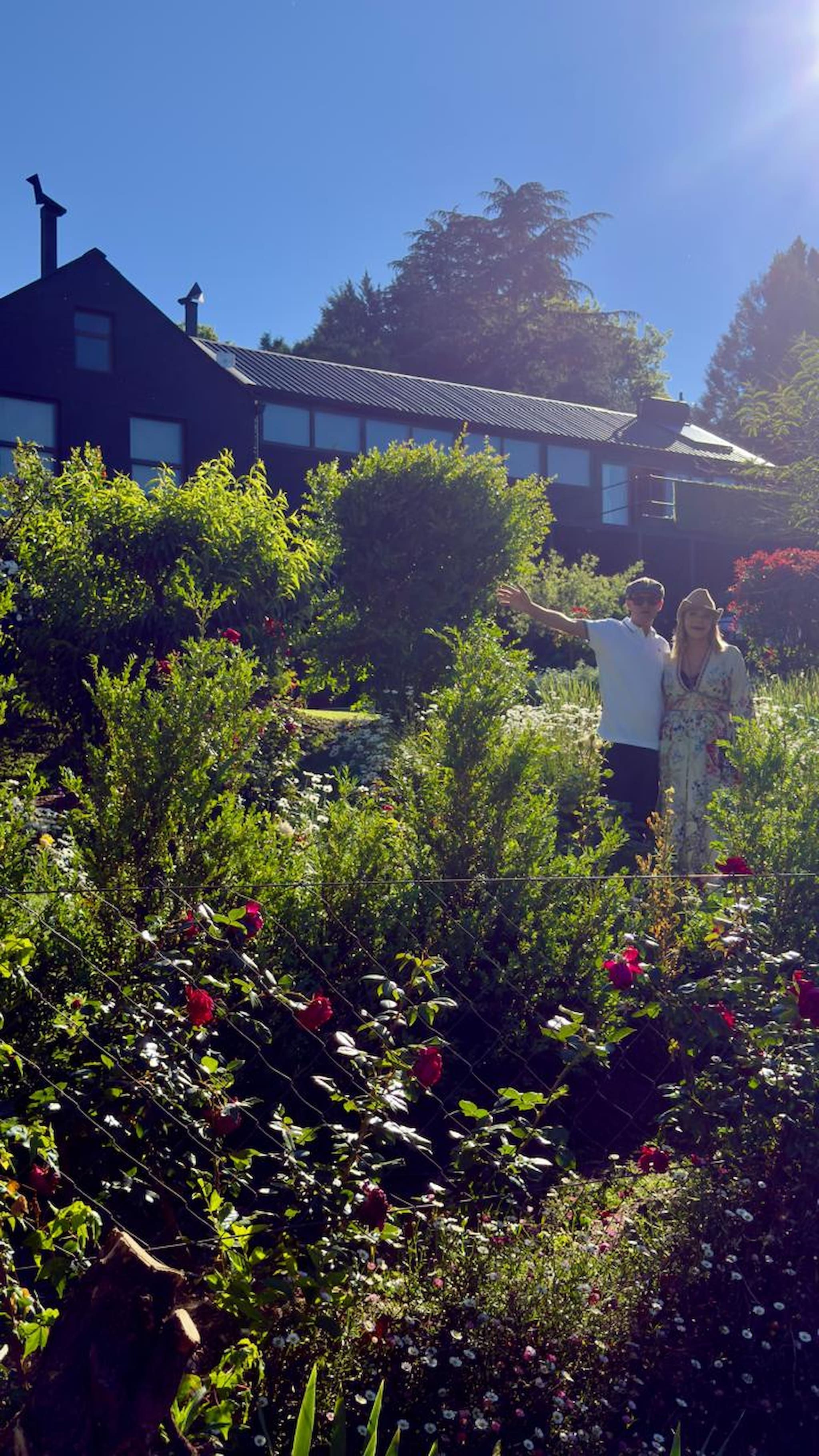 Un jardin avec différentes plantes et fleurs, un bâtiment doté d’un toit en pente et un ciel bleu dégagé.