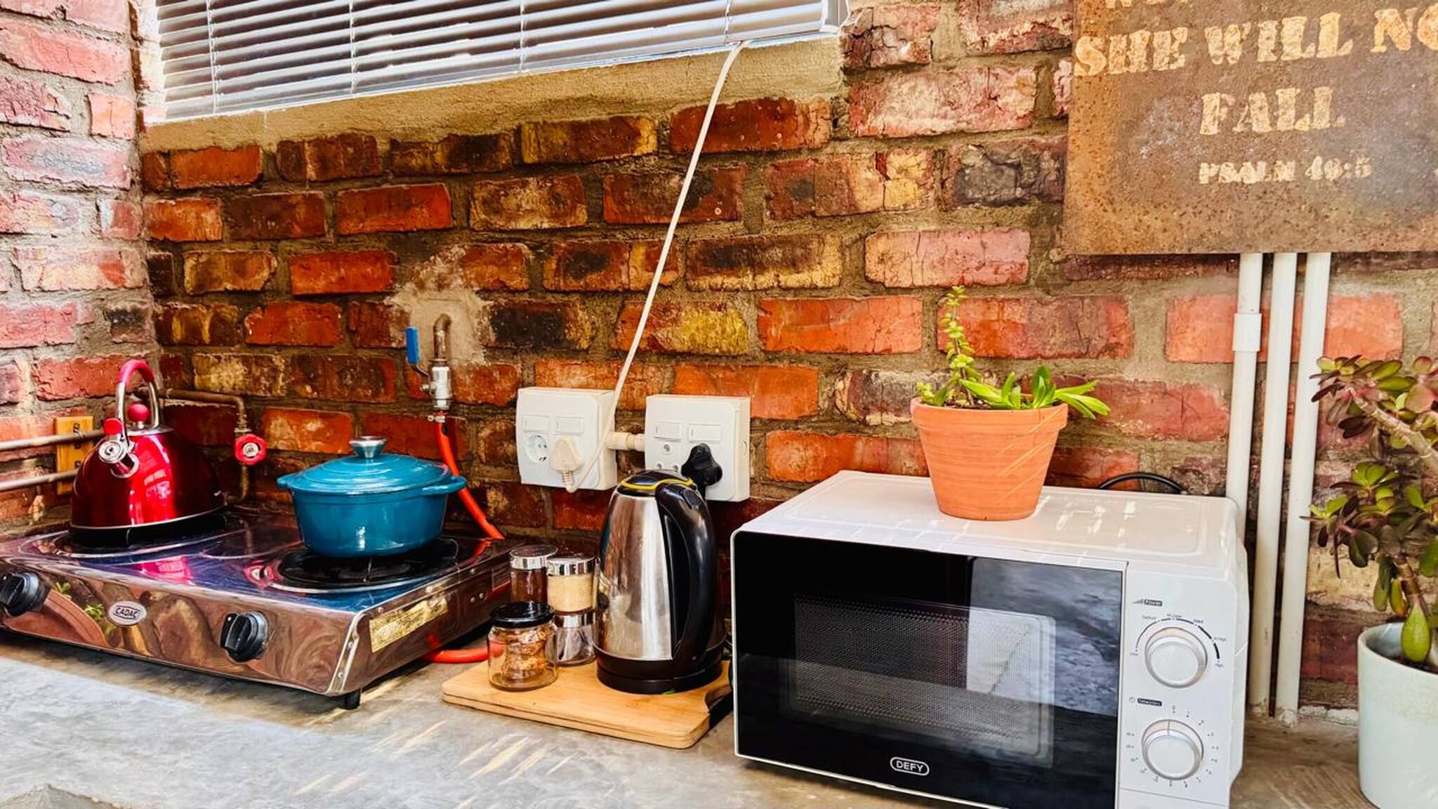A kitchen with a brick wall, a kettle, a pot, a microwave, and a sign with a biblical quote.