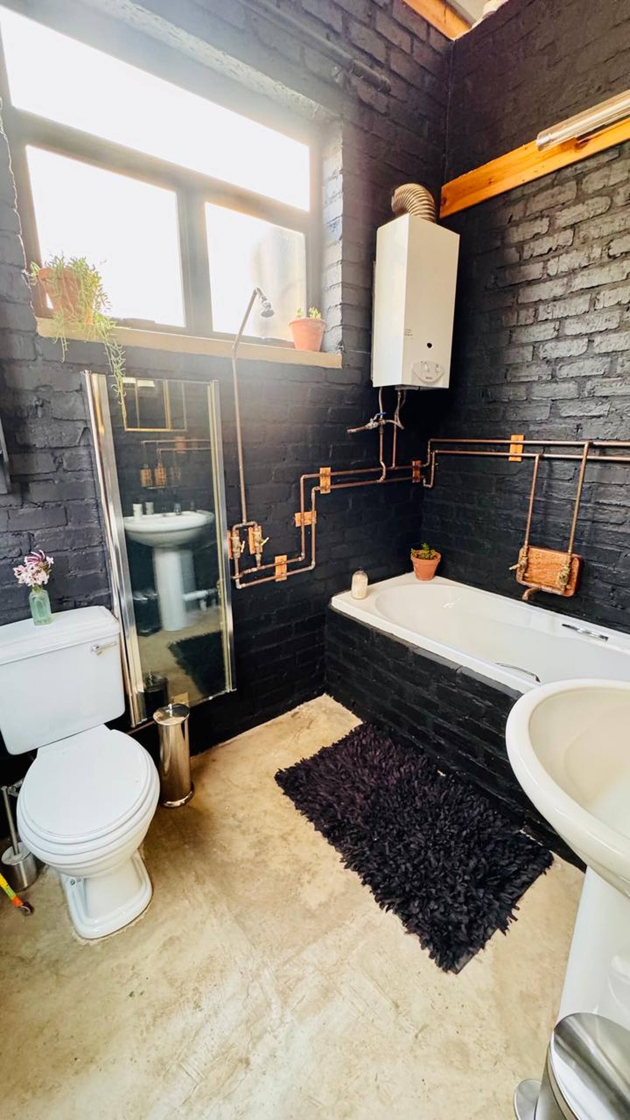 A modern bathroom with a black brick wall, a white toilet, a bathtub, and a sink.