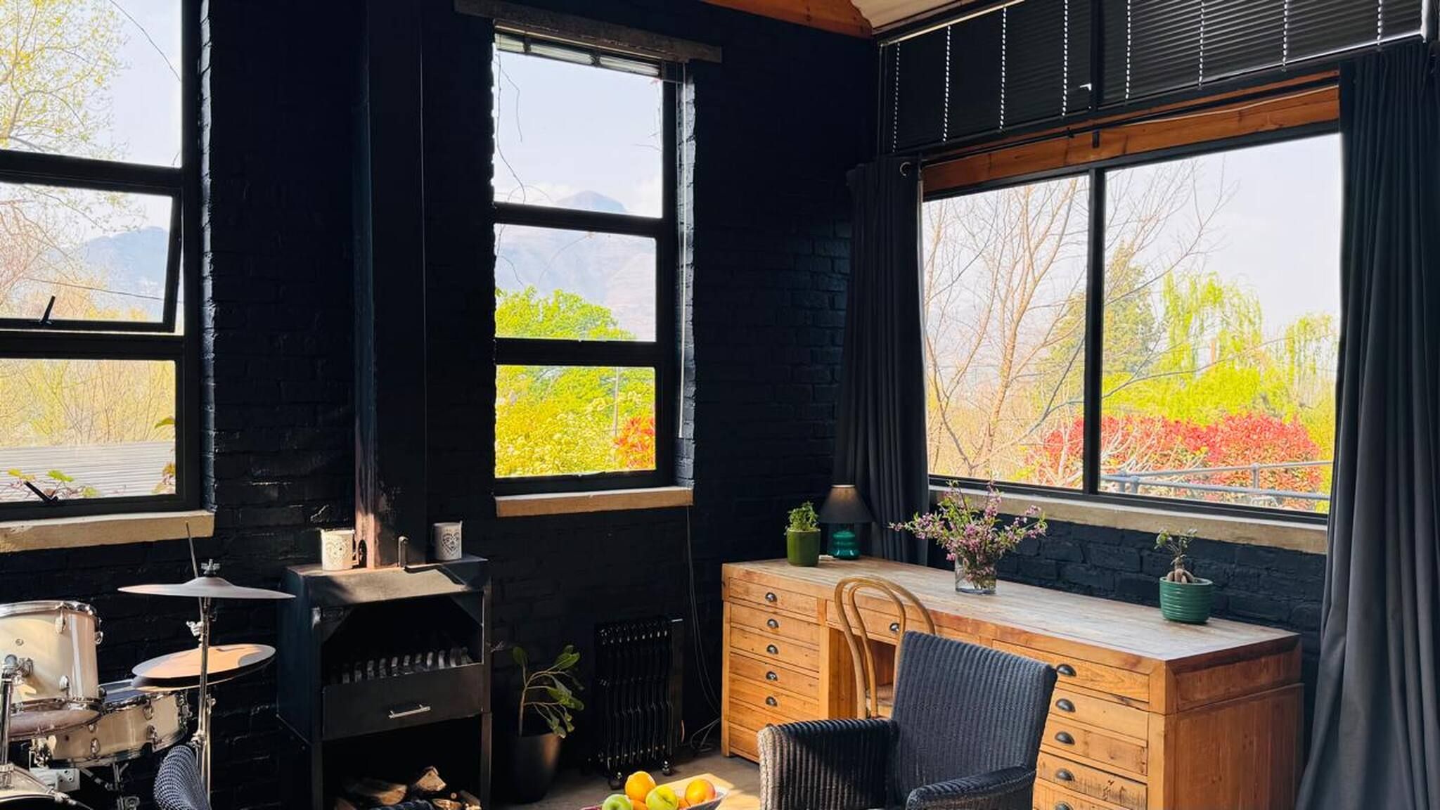 A room with a drum set, a radiator, a wooden desk, and a chair.