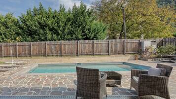 A swimming pool with stone flooring, surrounded by wicker chairs and a wooden fence.