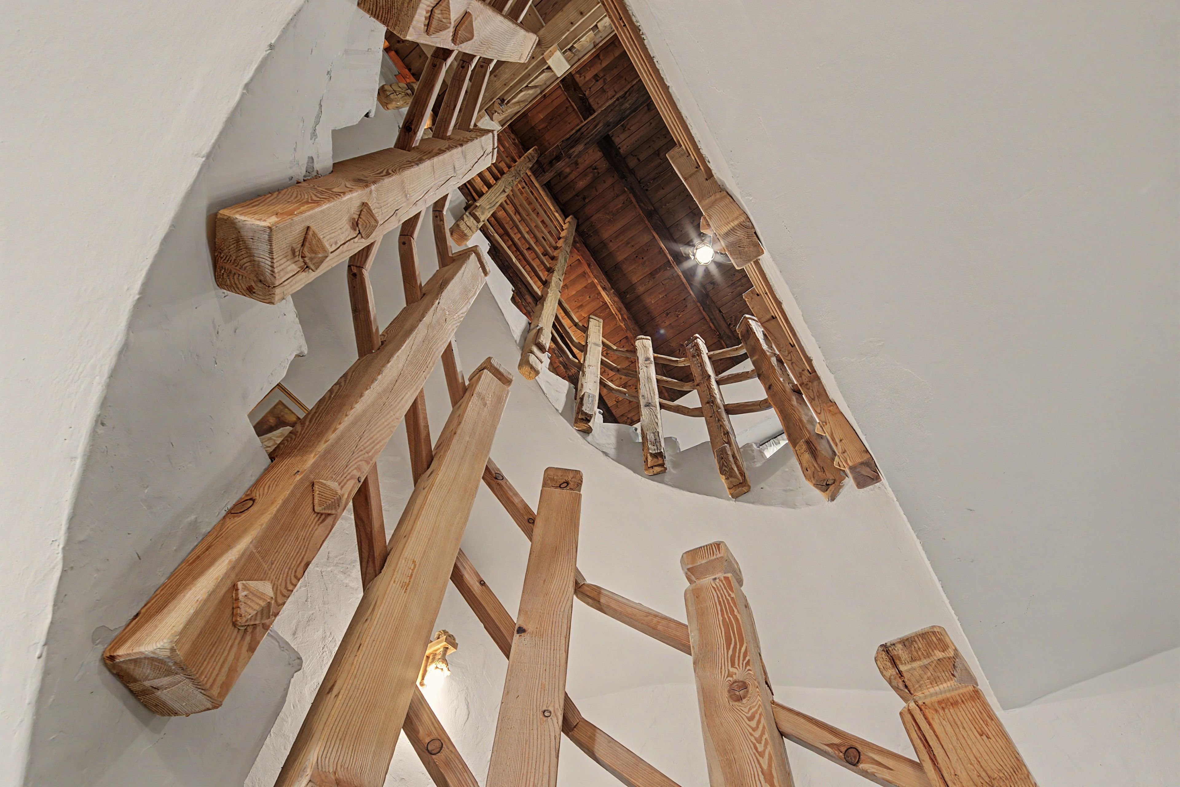 Un escalier en colimaçon avec des marches et des rampes en bois, qui monte jusqu’à un plafond également en bois.