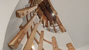 Un escalier en colimaçon avec des marches et des rampes en bois, qui monte jusqu’à un plafond également en bois.
