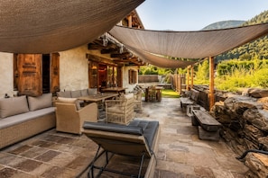Un patio al aire libre con suelo de piedra, mobiliario de mimbre y una pérgola de madera que ofrece sombra.