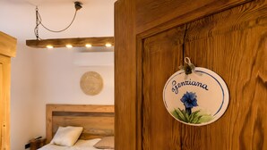 Een slaapkamer met een houten hoofdbord, een bed met witte beddengoed, een hanglamp en een rond bord aan de muur met een bloem en tekst.