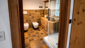 Een moderne badkamer met een glazen douchecabine, een bidet en een houten wastafelmeubel.