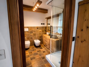 Un baño moderno con cabina de ducha de vidrio, un bidé y un mueble de tocador de madera.