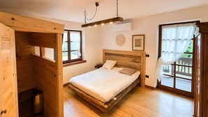 Une pièce avec un lit en bois, une fenêtre avec des rideaux, un luminaire au plafond et une petite poubelle.