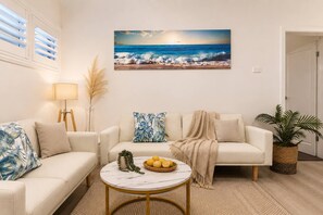 A living room with a white sofa, a round coffee table with lemons, and a beach scene painting on the wall. - Coastal Cottage Getaway | Blue Bay, Central Coast (Blue Bay)