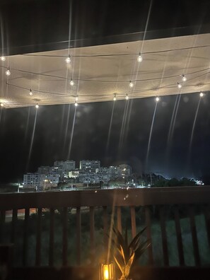 A balcony with a view of a cityscape at night, string lights overhead, and a potted plant in the foreground. - Your dream marina-front getaway is waiting for you (Fajardo city)
