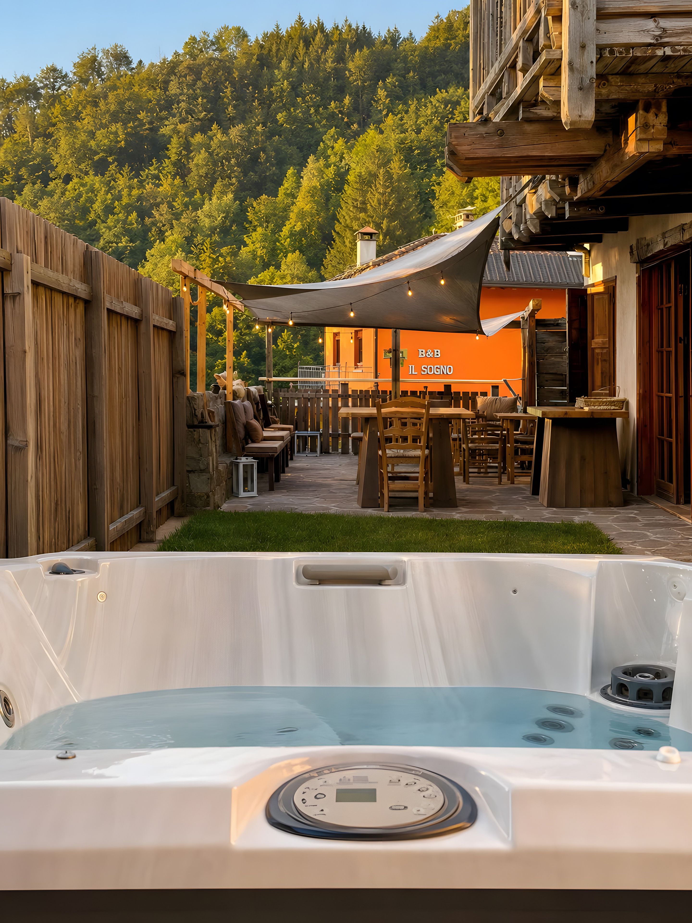 Una vasca idromassaggio in un giardino privato con recinzione in legno, area relax esterna e un edificio con facciata arancione sullo sfondo.