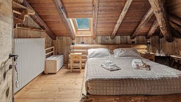 Une chambre confortable située sous les toits, avec un plafond en pente, des murs en bois, un lit avec des oreillers, une table de chevet et une commode, ainsi qu’une fenêtre.