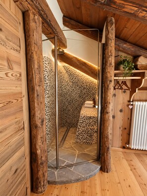 A wooden interior with a stone-tiled shower area, wooden beams, and a radiator.