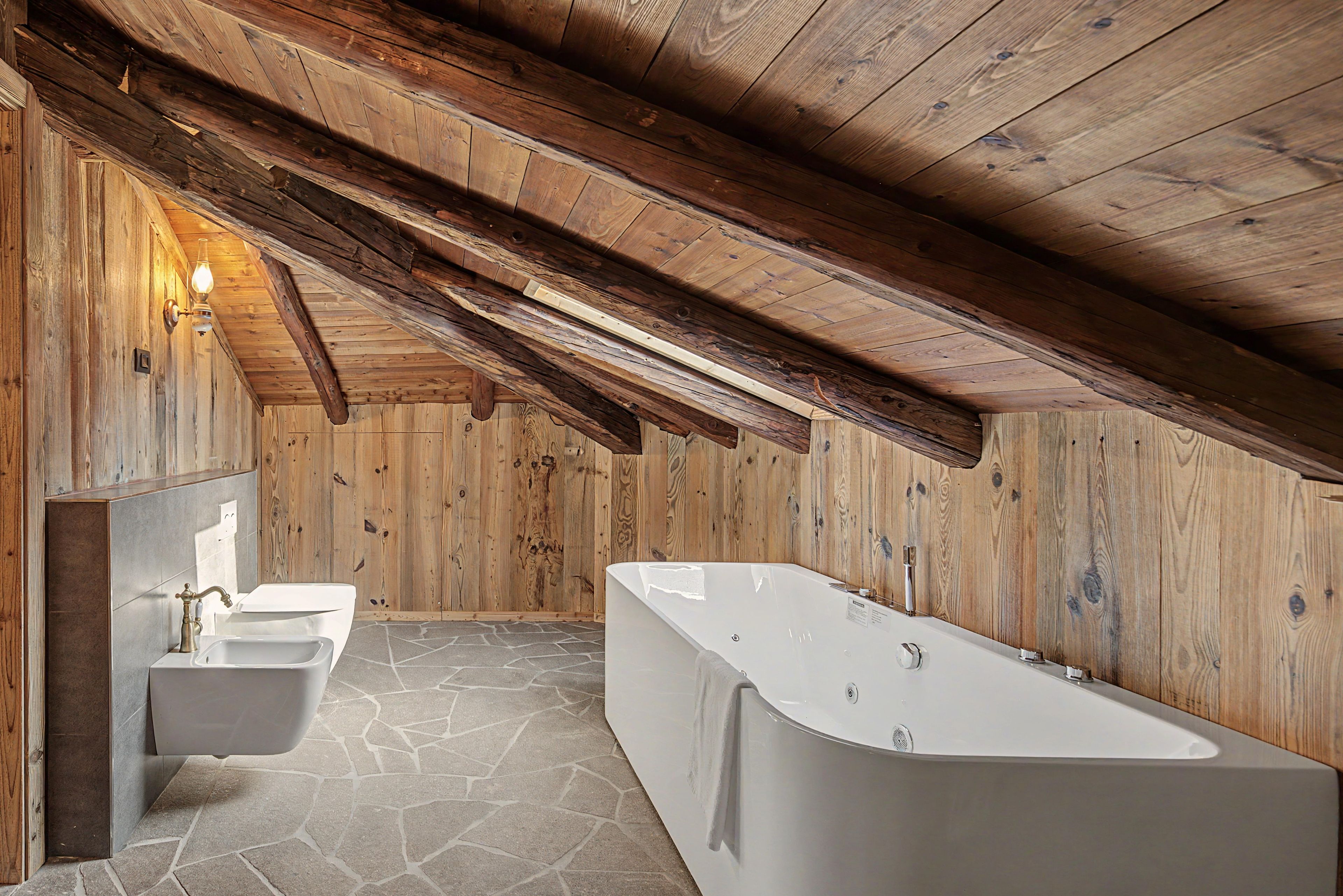 Une salle de bain avec un sol en pierre, une baignoire sur pieds et un lavabo fixé au mur.